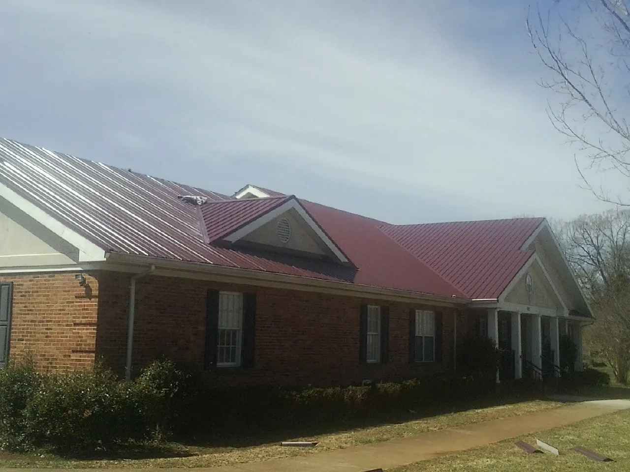Red metal roof with gabled entries on a long brick building, from a Hail Damage Roof Repair job in Tooele