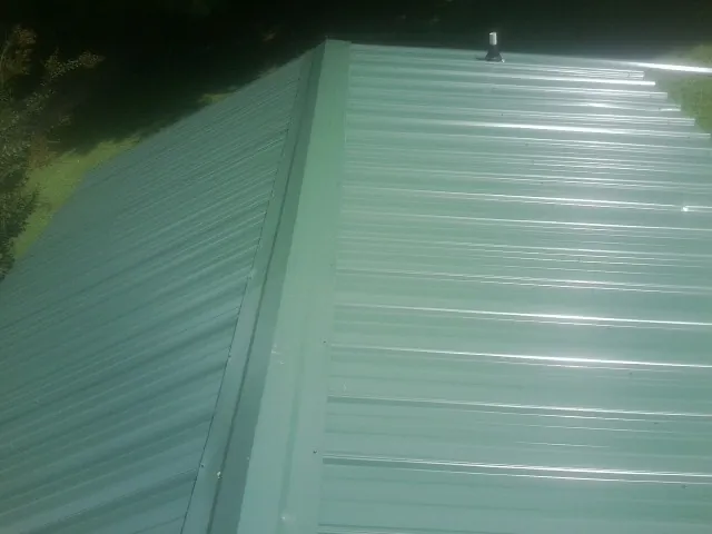 New green metal panels meeting at the ridge of a roof — Flat Roof Repair work by our crew in Tooele