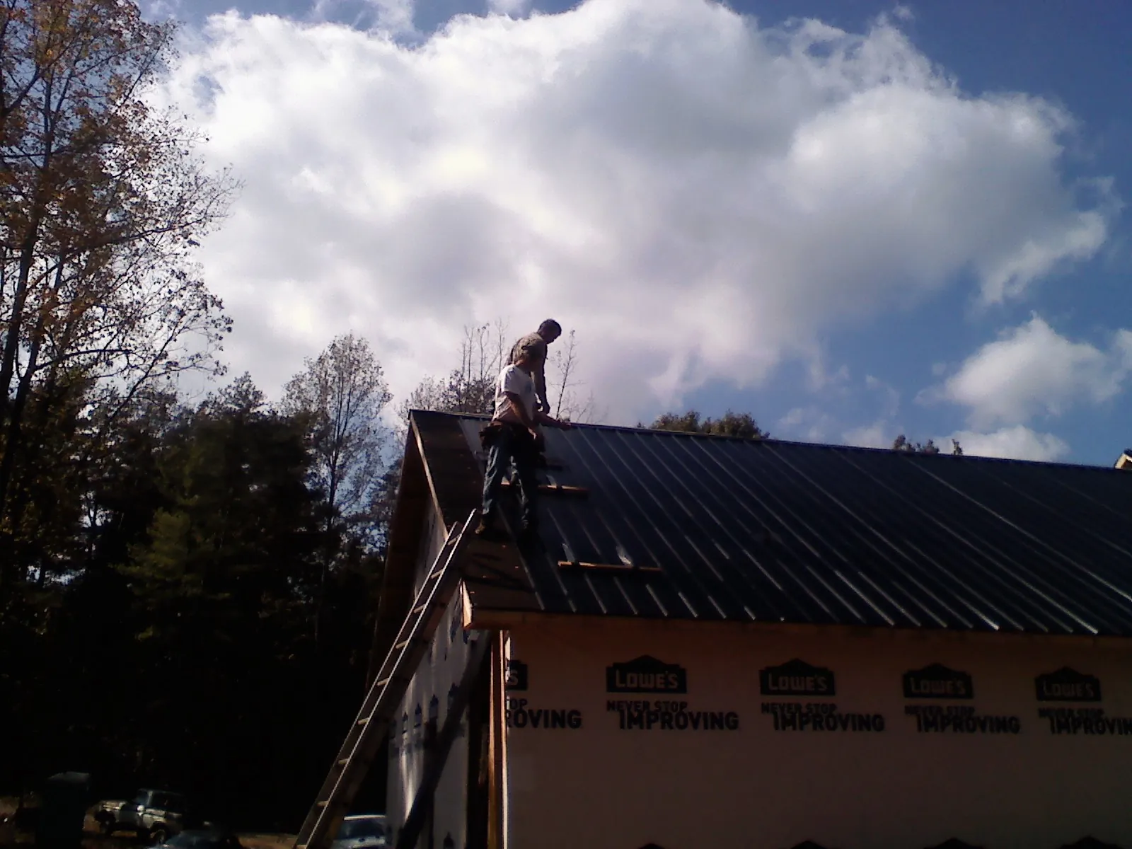 Roofer fastening dark metal panels high against a cloudy sky, from a Roof Inspection job in Tooele