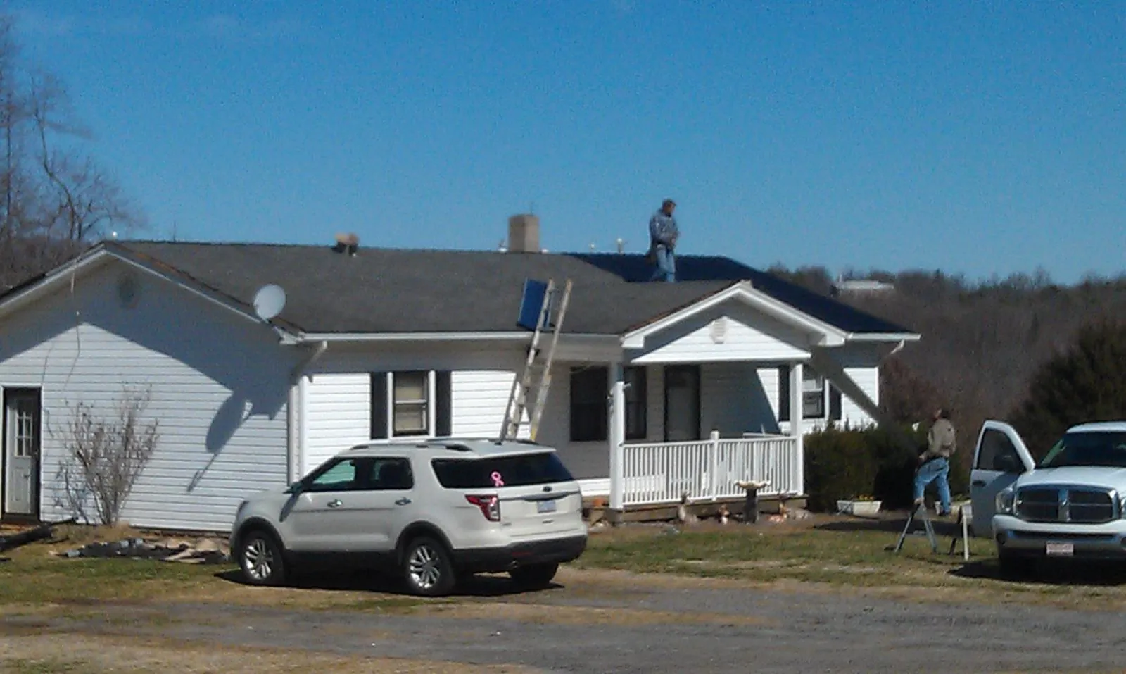 Roofers stripping shingles from a white ranch house roof in Tooele