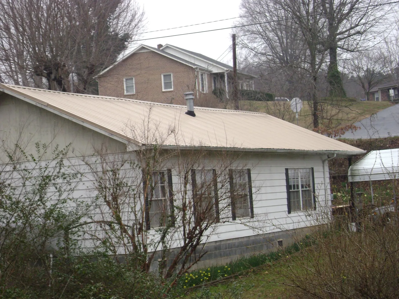 Tan metal roof on a white sided house set into a hillside — Commercial Roofing by Roofing Brothers in Tooele